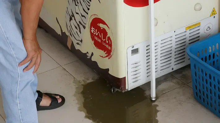 Seorang pelanggan melihat genangan air di bawah chiller es krim, sebuah tanda yang menunjukkan perlunya segera dilakukan service chiller es krim untuk mencegah masalah lebih lanjut."